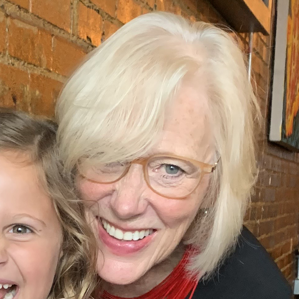 Close-up of Cathy Smith smiling and hugging a small, laughing child from behind.