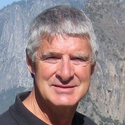 Close up of Rich Fisher wearing a black shirt, shown outdoors with a mountain scene in the background.